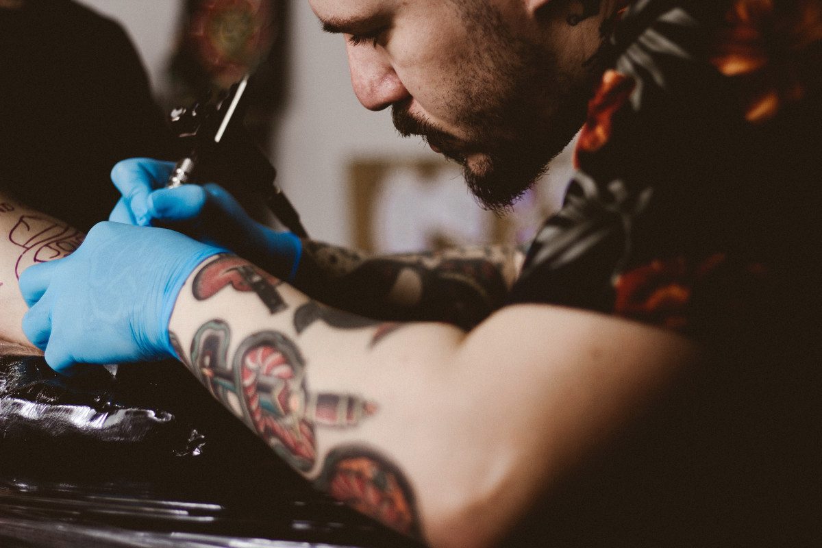 Tattoo artist in blue gloves working on a colour piece