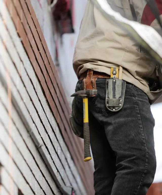 Roofing crew member with a tool belt and hammer working alongside fresh siding boards