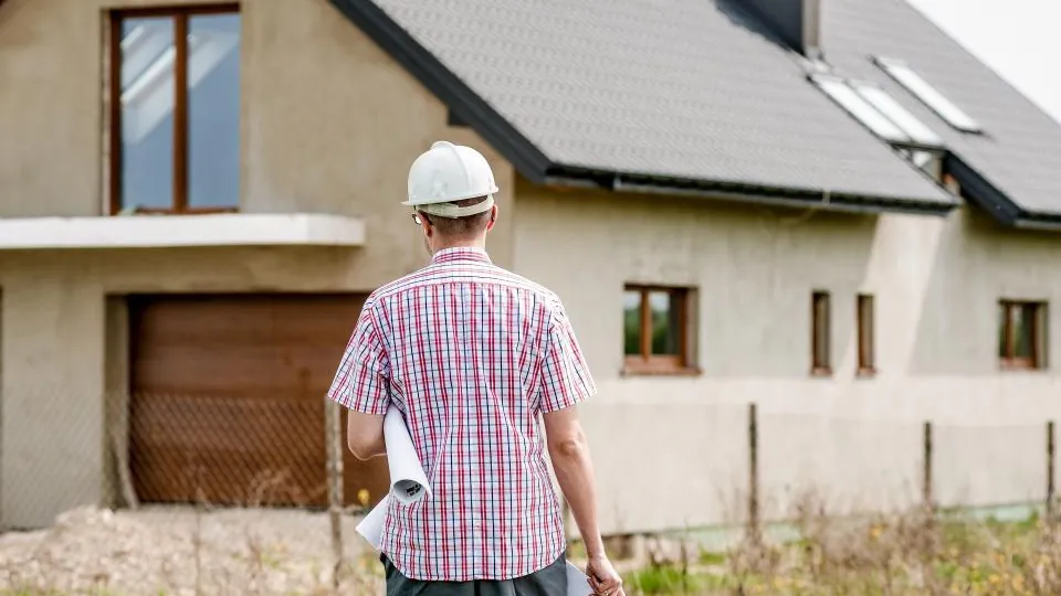 Roofing contractor in a hard hat reviewing plans in front of a house with a newly finished roof